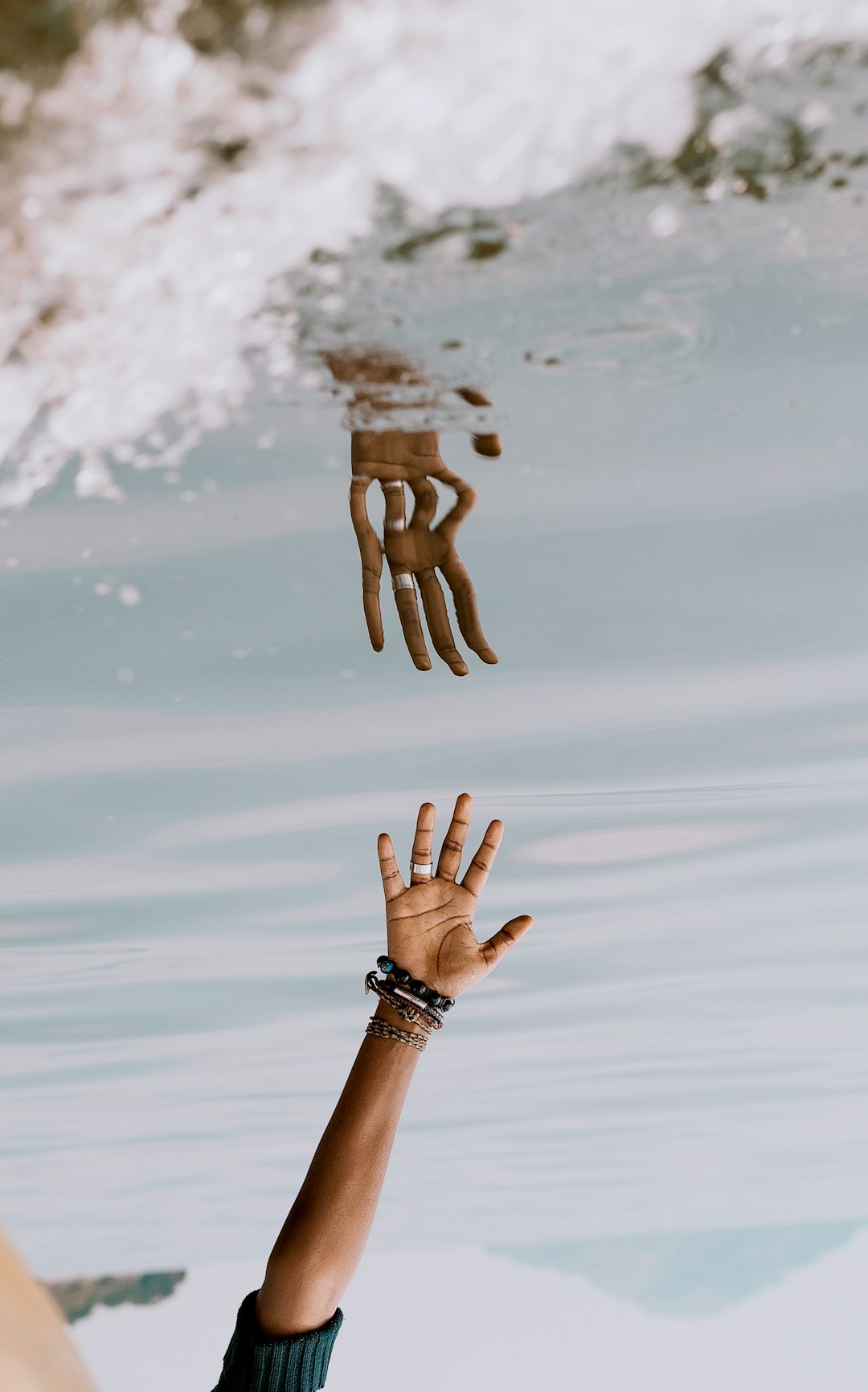 person\'s hand reaching on water with reflection ]