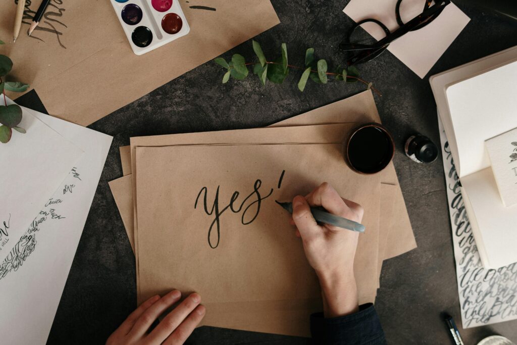 Artistic calligraphy session featuring the word 'yes!' with natural eucalyptus accents.